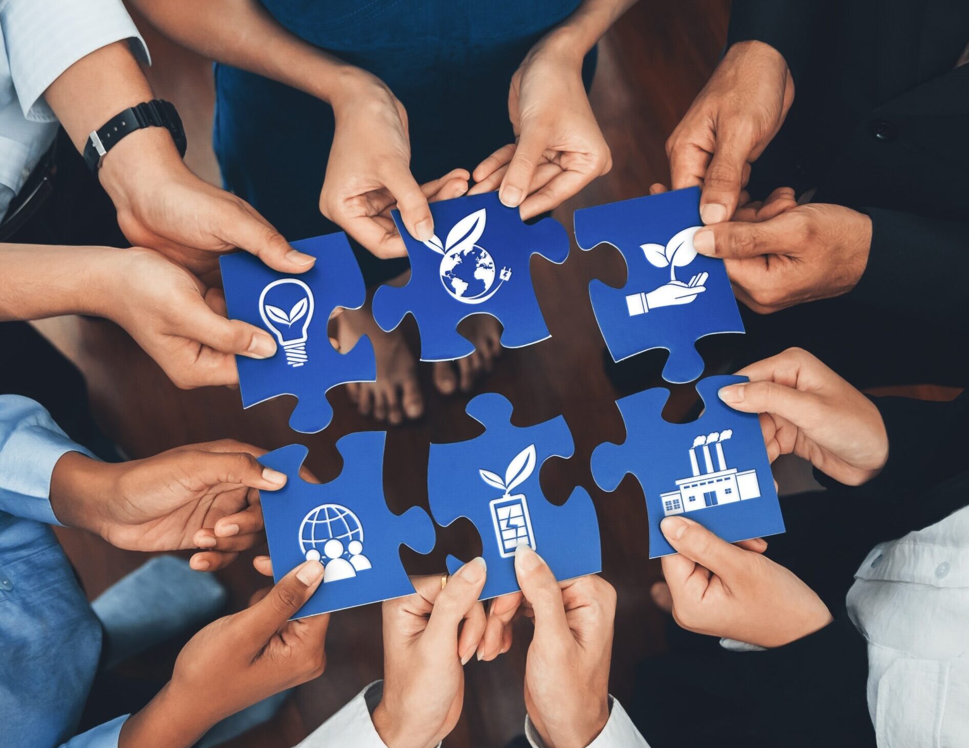 cerchio di persone che tiene in mano un pezzo di un puzzle di colore blu con sopra delle icone rappresentative della sostenibilità e impegno sociale